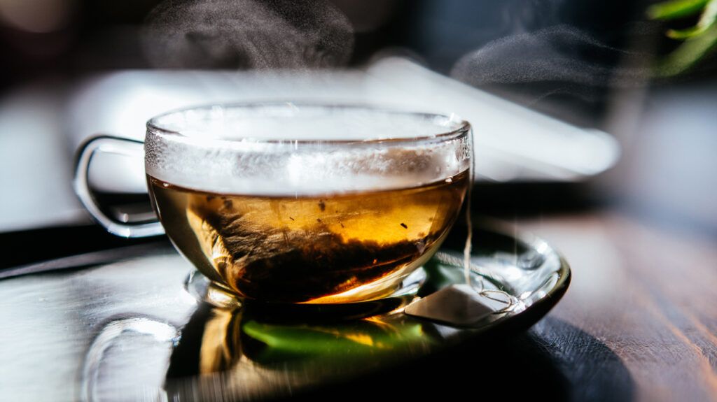 Transparent teacup containing a light tea that could be a natural remedy for asthma. The teabag is visible through the teacup and steam is coming from the top