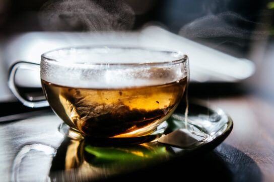 Transparent teacup containing a light tea that could be a natural remedy for asthma. The teabag is visible through the teacup and steam is coming from the top