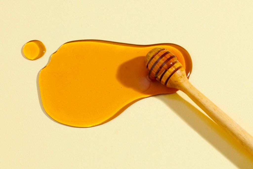 Spilt honey on a surface with a honey dipper.