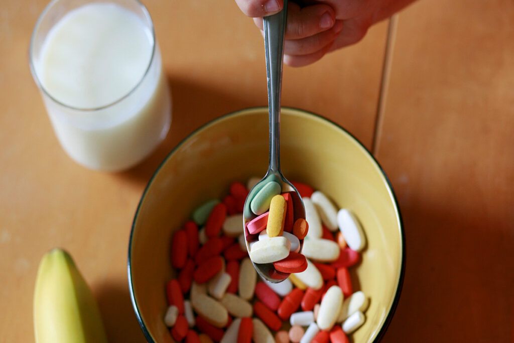 A bowl of vitamins with a glass of milk