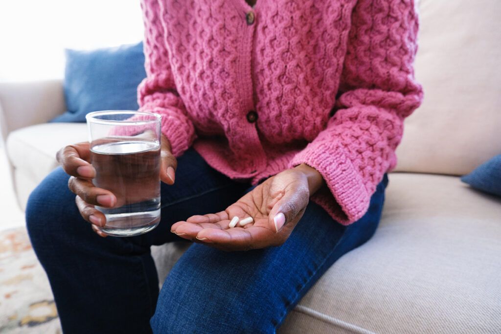 A person holding pills in one hand and a glass of water in the other