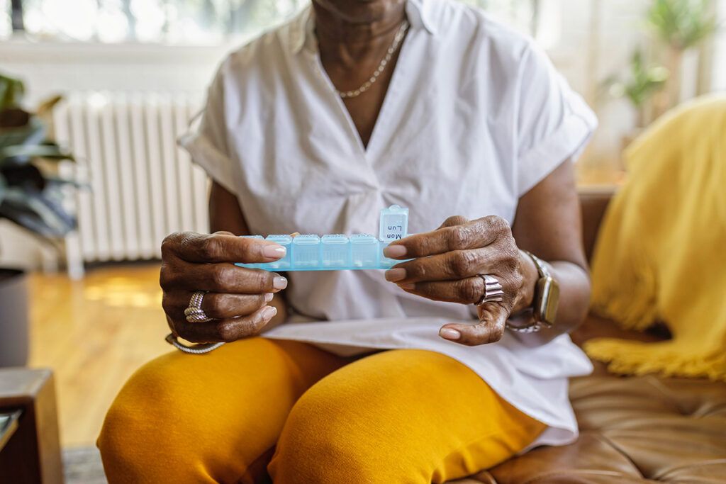 A person sitting down opening a pill box.