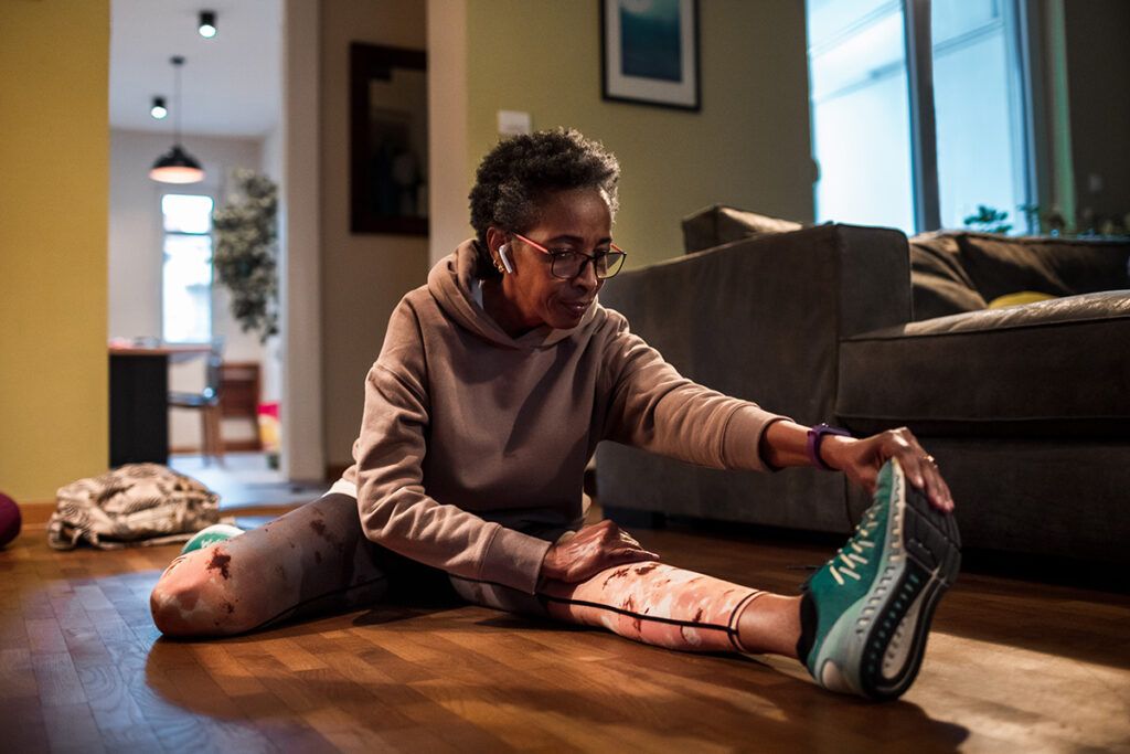 A person in sports clothes stretching on their living room floor