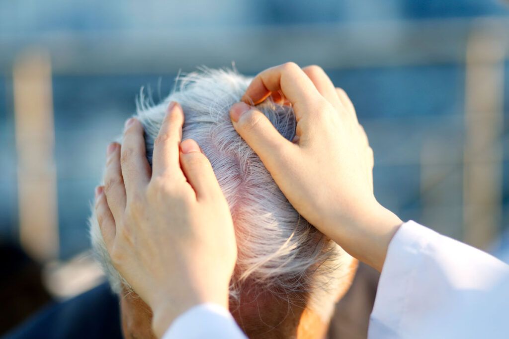 A person checking an older adult's scalp, looking through their hair.