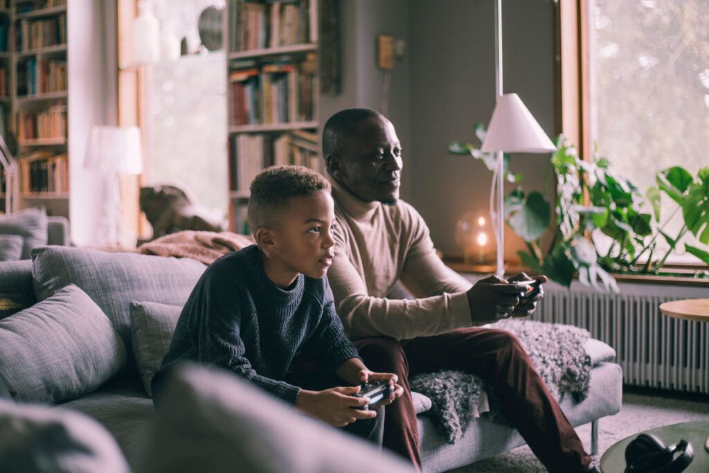 An adult and a child on a couch together playing a video game