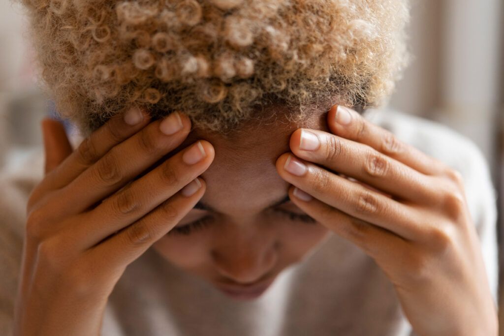 adult female with head bowed and forehead resting on their fingers as if to ease a headache and they could be considering botox for migraine 