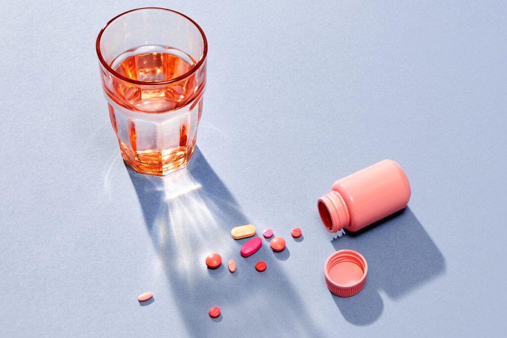 Half full glass of water with an open pill bottle next to it. The pills are spilling out next to the glass. The water denoting a better choice than antidepressants and alcohol