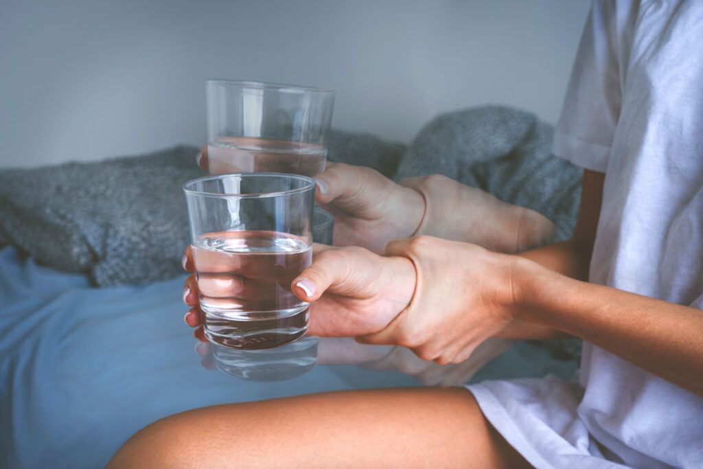 An image of someone grasping the wrist of their right hand to steady a tremor, whilst also holding on to a glass of water.