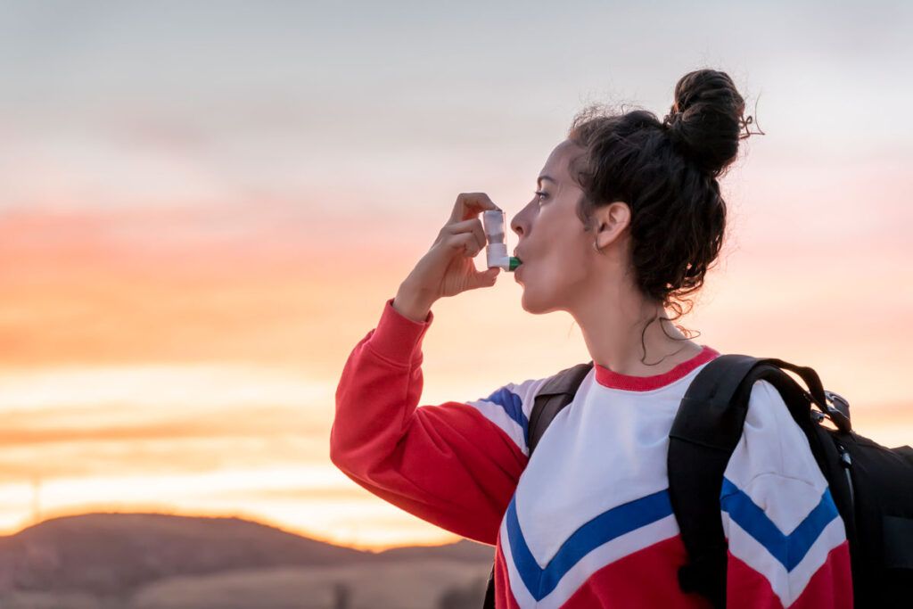 A person using an inhaler while walking in nature