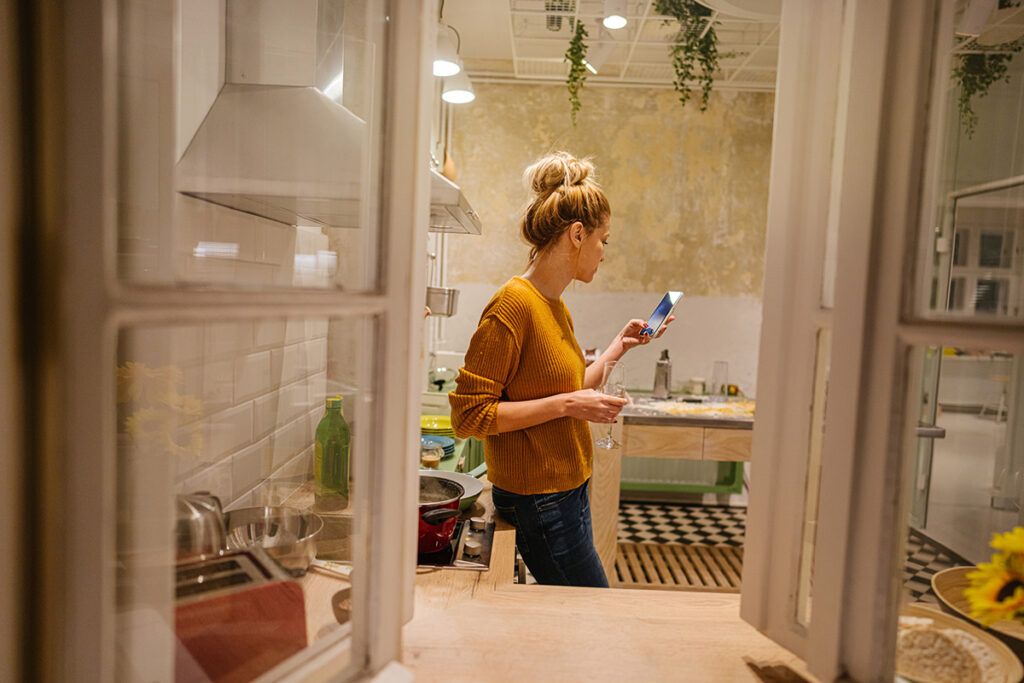 An image of someone standing in the kitchen, holding a glass of alcohol.