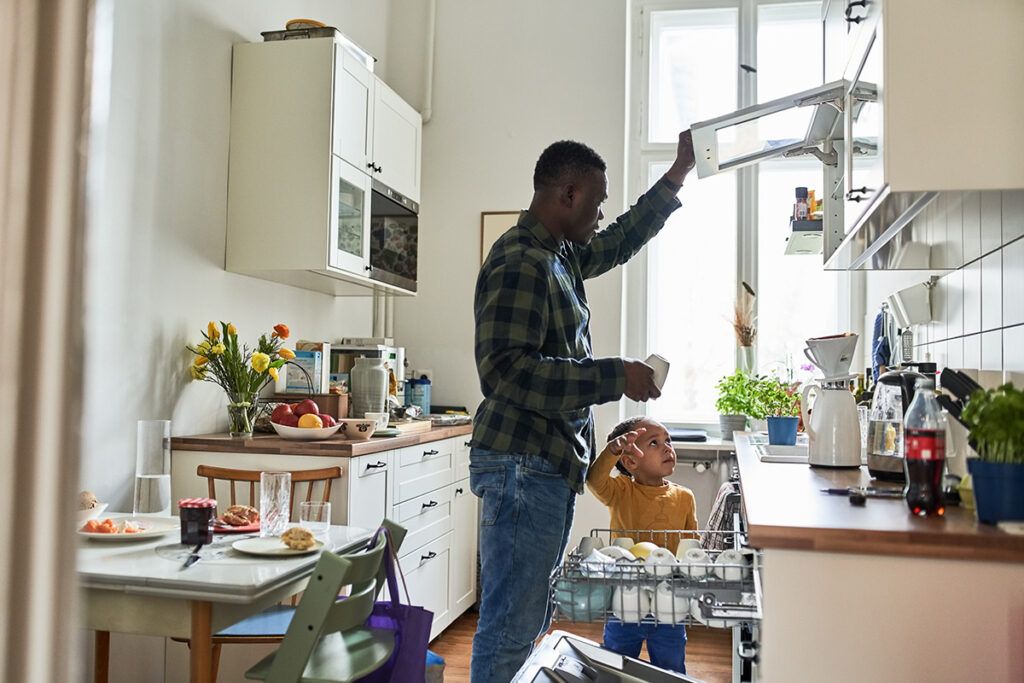 Adult Black American male multitasking in his home kitchen while watching his toddler depicting hypertension in African Americans