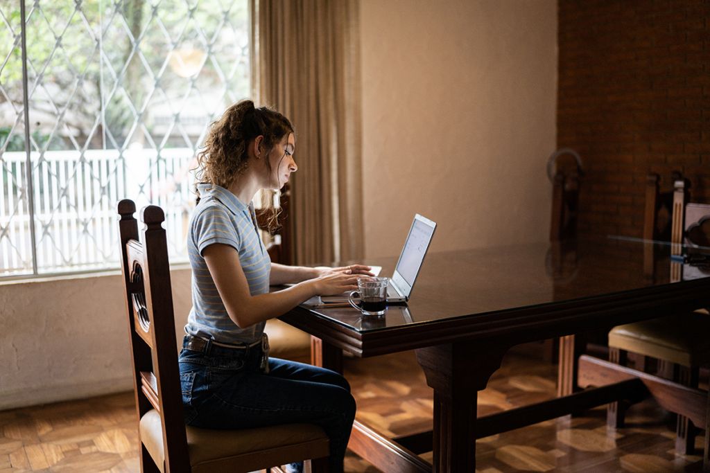 A young person sitting at a table looking at a laptop.