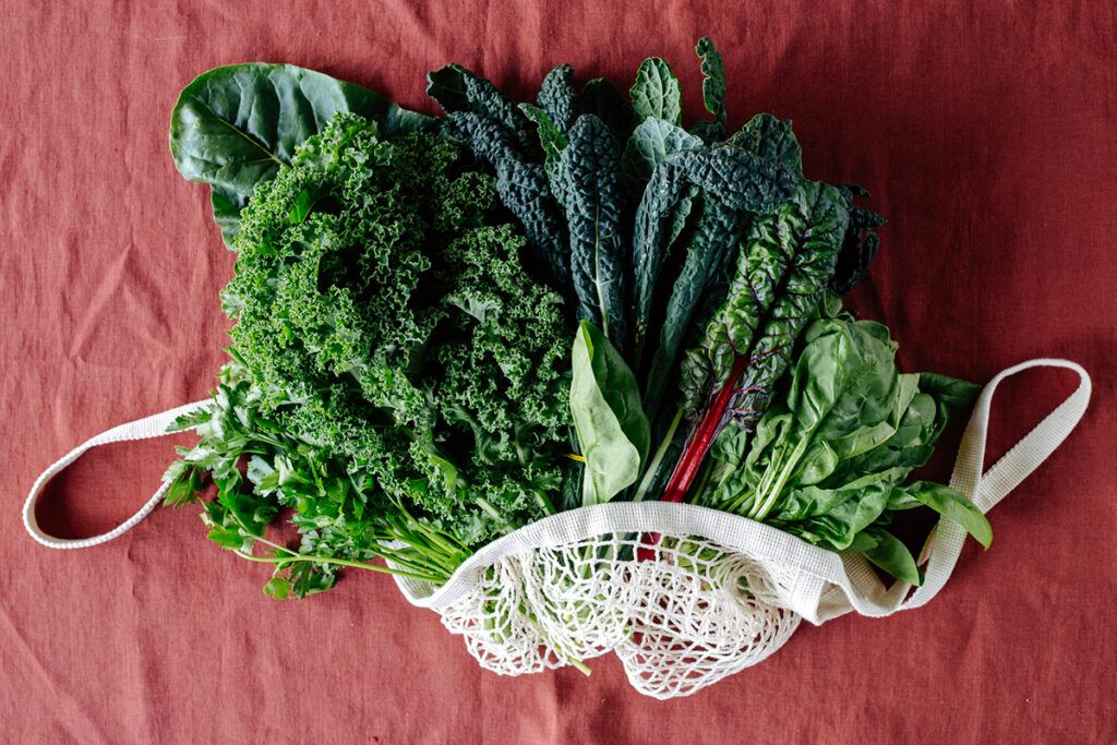 An arrangement of leafy green vegetables protruding from a loosely woven shopping bag depicting nitric oxide benefits
