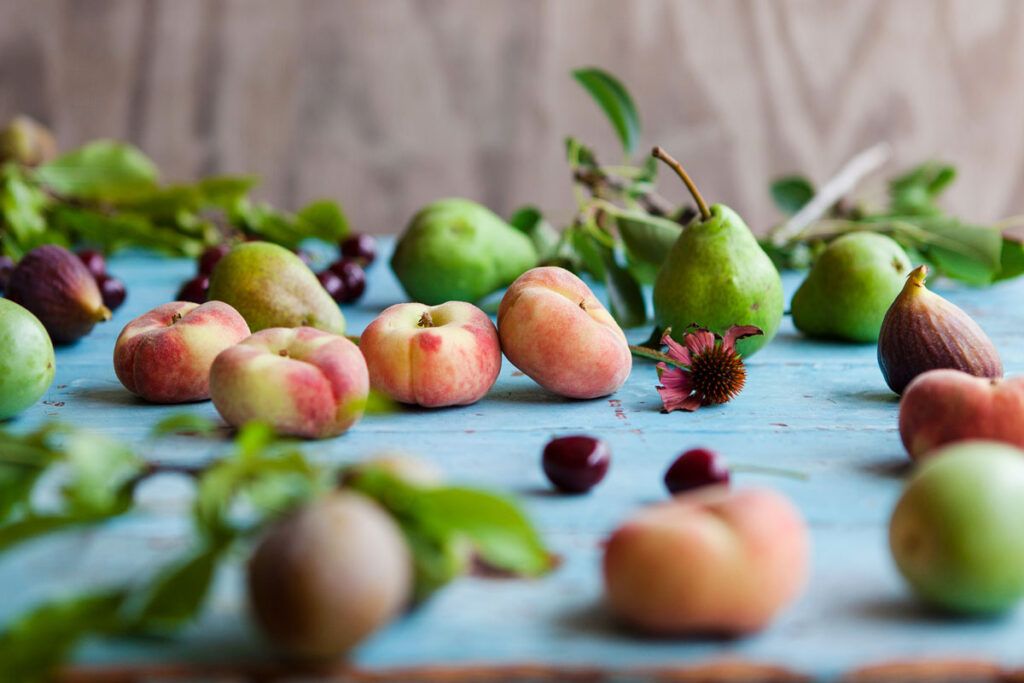 Several peaches, cherries, and pears scattered over a blue surface.