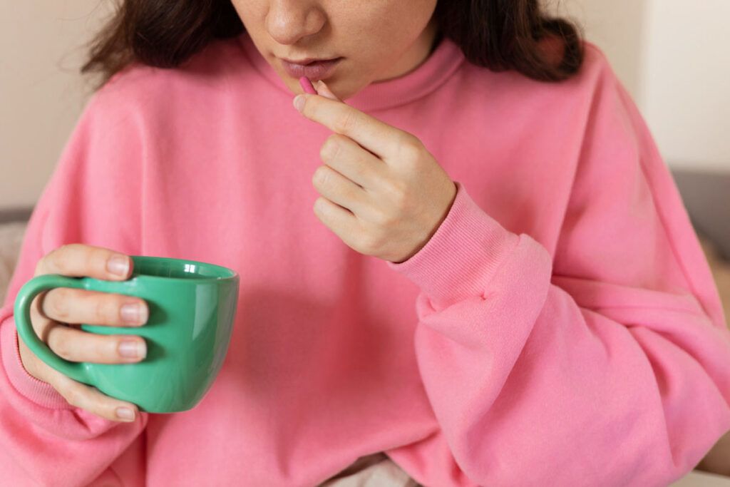 Adult female taking an Adderall pill with a mug of coffee, wondering about the effects of Adderall and caffeine