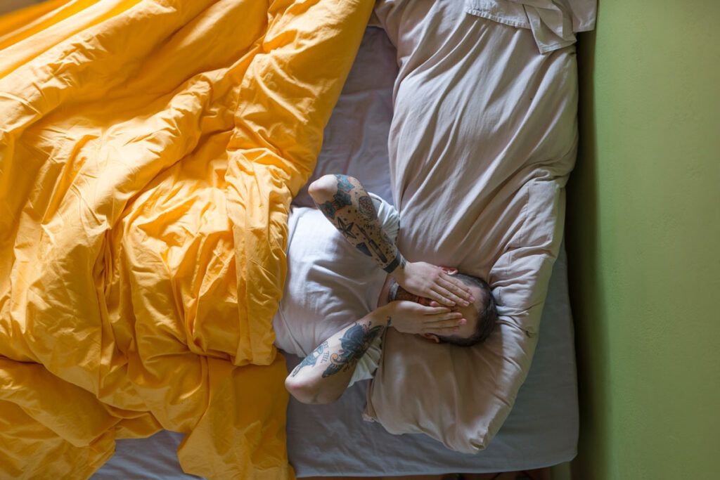 A person in bed with their hands over their face.