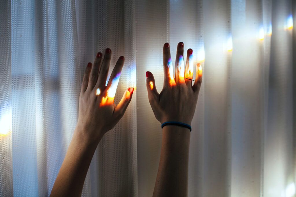 Hands against a curtain with rainbow lights projected onto them