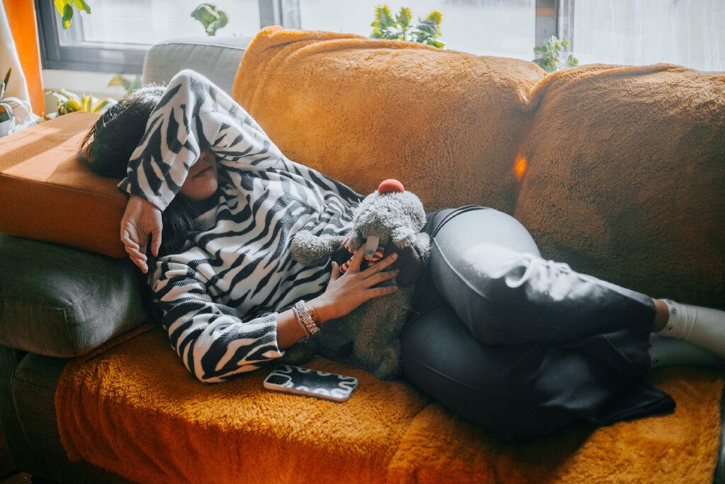 A woman lying on a couch holding a hot water bottle to her abdomen to represent ovary pain.