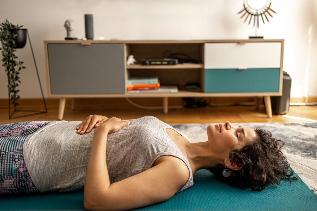 A person lying on the floor with their hands on their abdomen, representing breathing techniques.