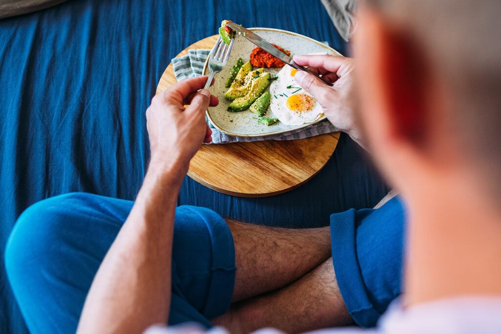 Person sitting cross legged eating from a plate of eggs and avocado.