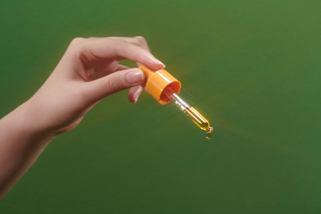 Hand holding dropper with essential oil from a mix of herbs for anxiety relief