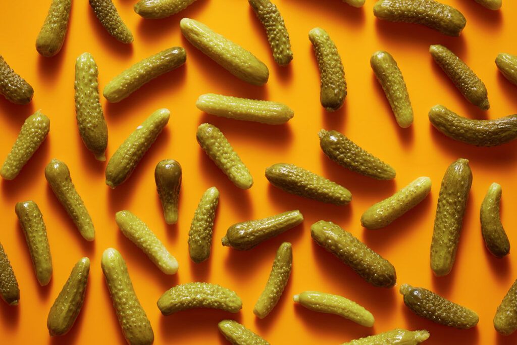 An image of tens of pickles scattered across an orange surface.