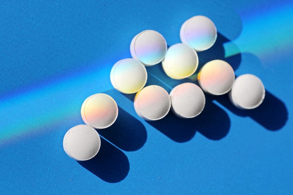 white pills on a blue background with a rainbow prism of light representing does ibuprofen raise blood pressure
