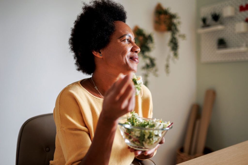 A middle-aged woman eating a salad, which is helpful in a fibromyalgia diet.