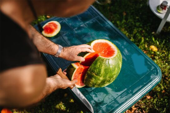 Close up of a person cutting into a watermelon in an outdoor setting possibly thinking about watermelon and diabetes