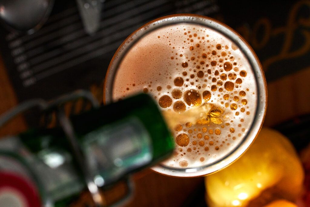 Close up of an overhead shot of a beer being poured into a glass from a bottle with lots of bubbles forming in the small amount of foam on the top depicting alcohol and Crohn's disease