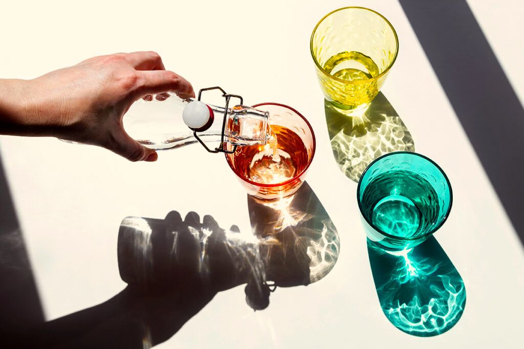 Overhead shot of someone pouring liquid into differently colored drinking glasses depicting a liquid diet to rest bowel symptoms