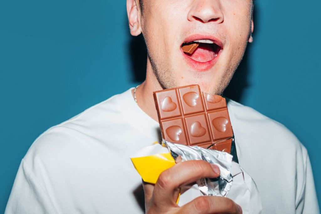 Male eating from a big bar of chocolate that has decorative hearts on it.