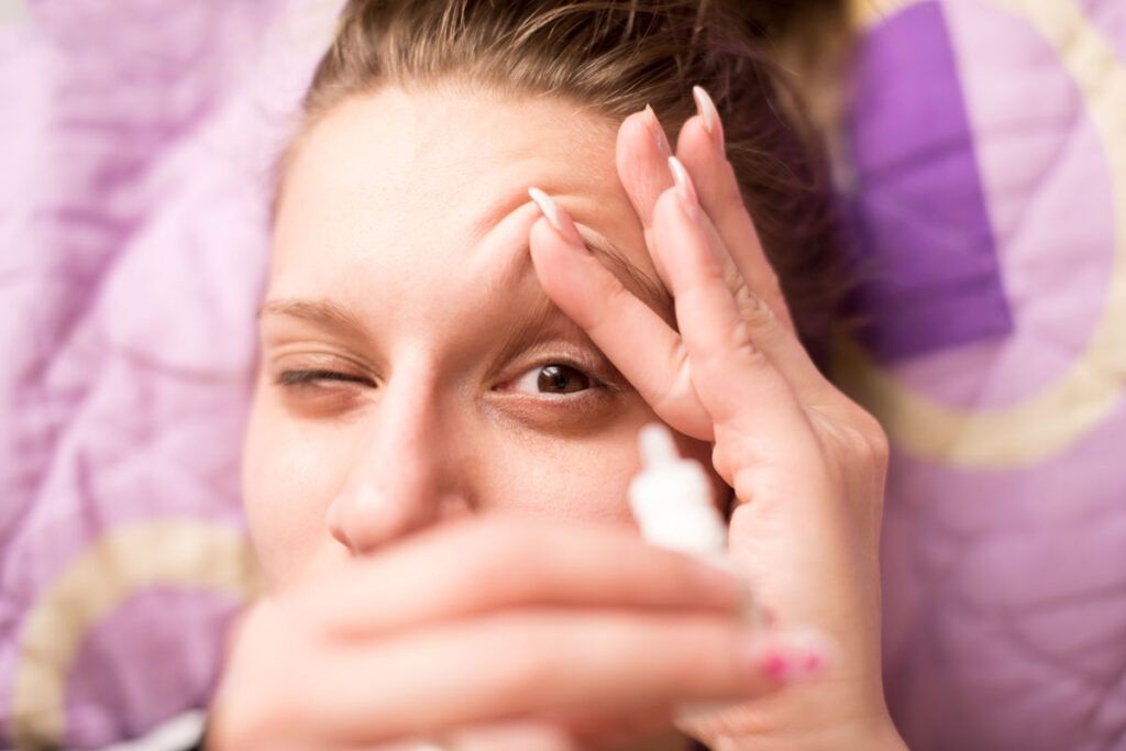 A person holding open their eye and preparing to use eye drops, because dry eyes cause blurry vision.