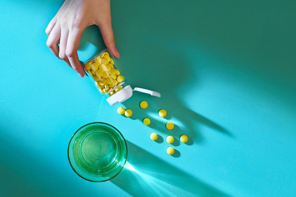 A hand pouring out a bottle of vitamin D pills onto a blue background, which can help with eczema.