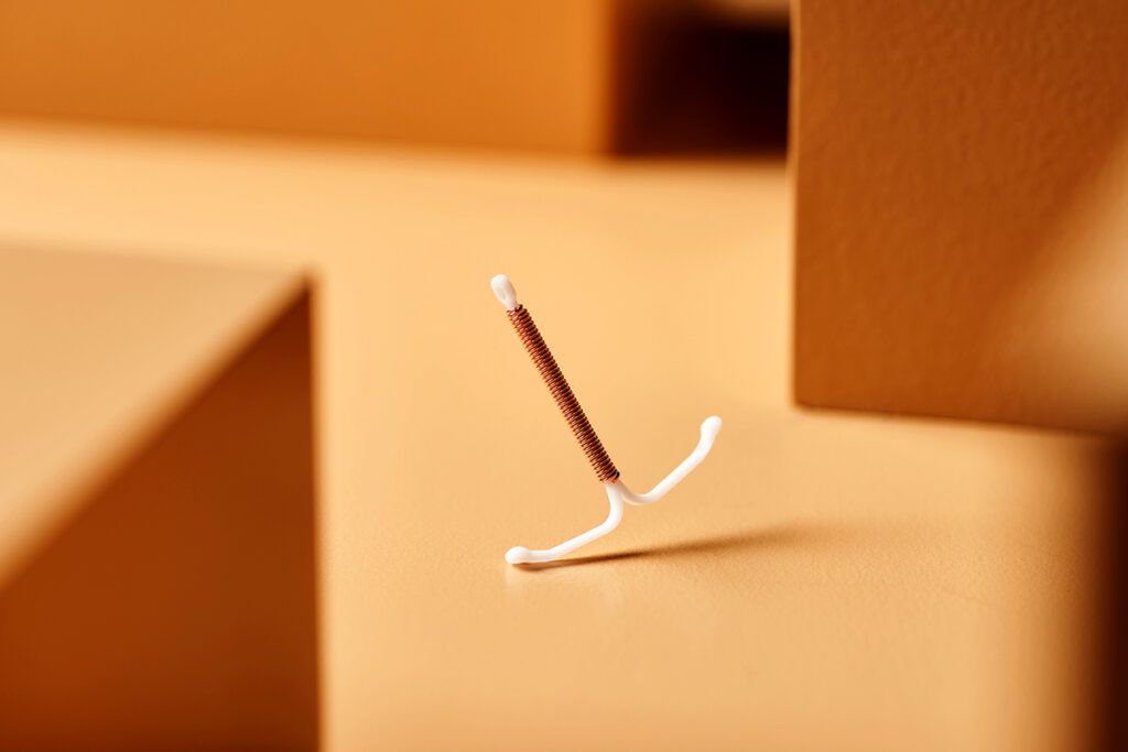 An IUD standing on one of its tips on top of a wooden surface with blurred boxes around it signifying can you feel an IUD during sex