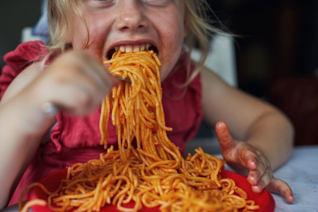 A child eating a big bowl of spaghetti representing whether there is a worst food for asthma