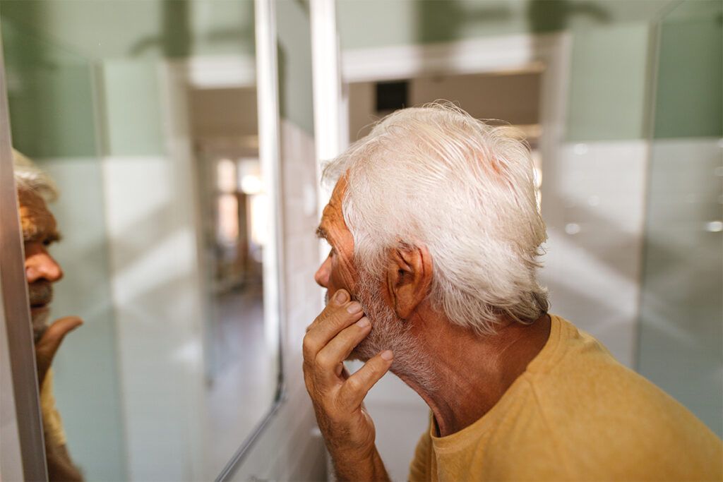 Older adult male looking in a mirror and inspecting his skin for what could be a Crohn's disease rash