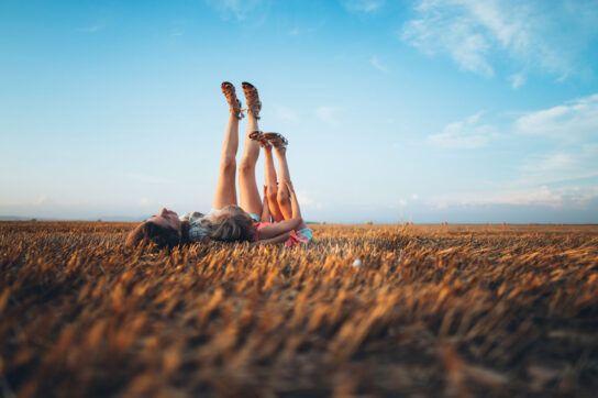 A mother and child laying on their backs in a field with their feet pointing toward the sky.
