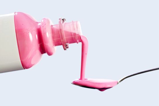 A bottle of pepto bismol being poured onto a spoon, a common diarrhea medication.
