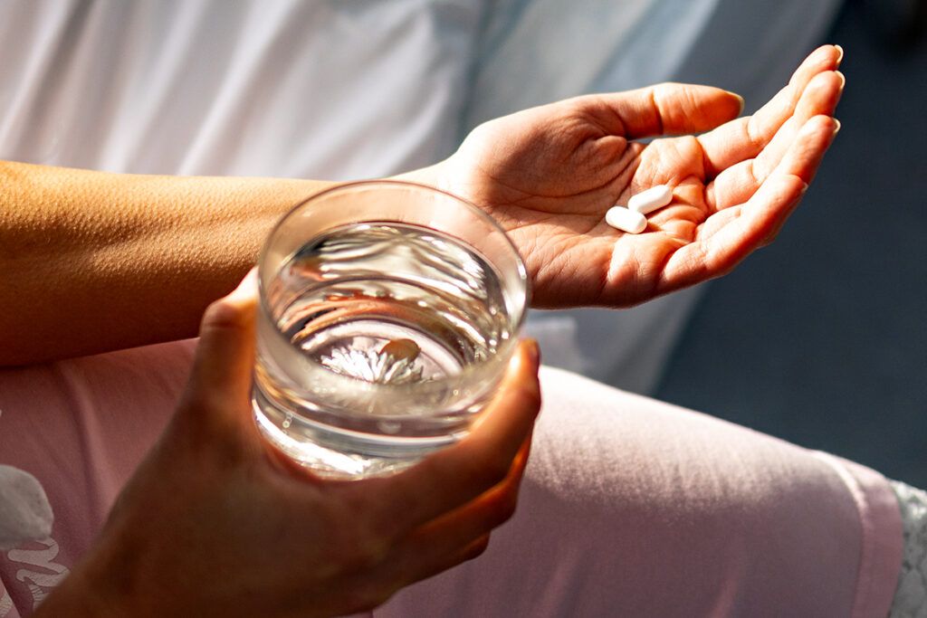 Person holding a glass of water and two pills of non-addictive anxiety medication