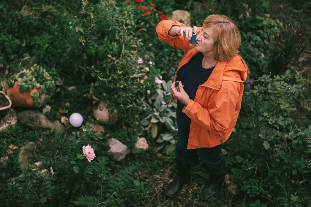 An older adult using an inhaler outside in a grassy area to relieve symptoms of seasonal asthma