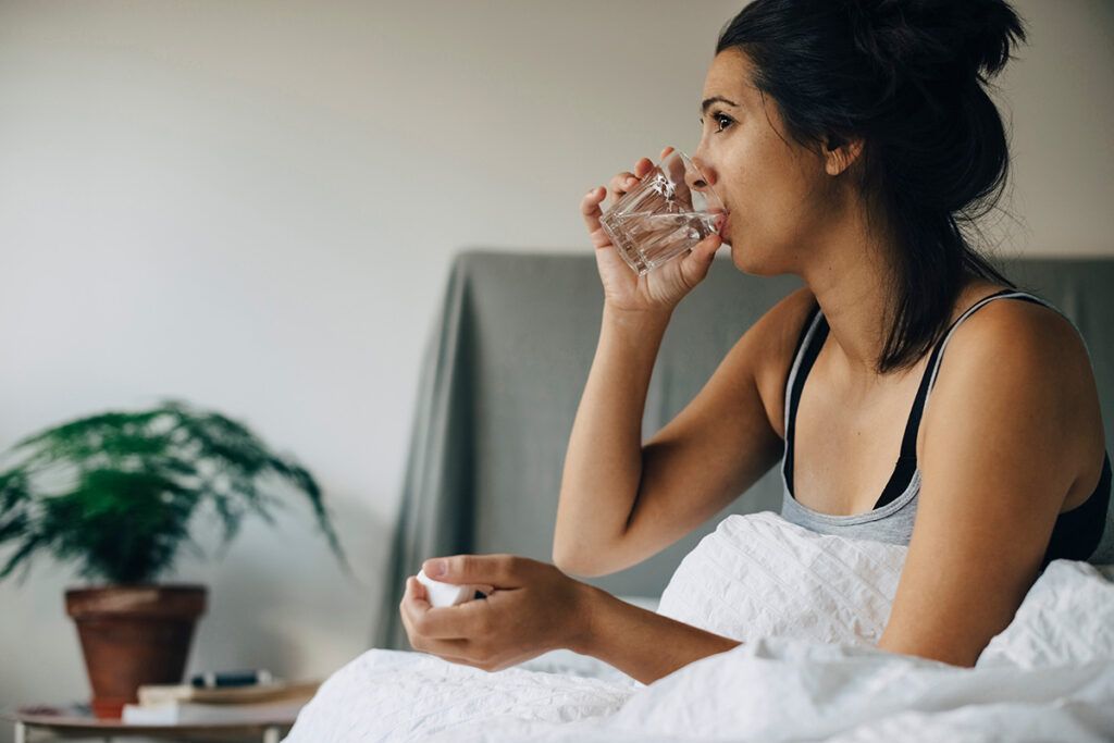 Female sitting up in bed and drinking a glass of water. 