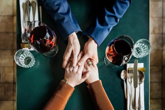 A couple holding hands across a dinner table, representing a discussion about HPV vs. HIV.