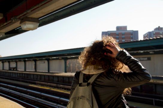 Person standing on a train platform with their hand in their hair.