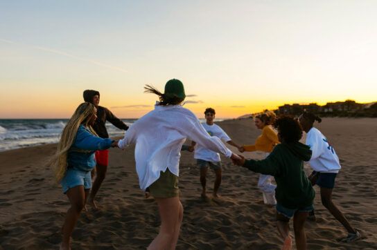 Young adults on a sandy beach at sunset holding hands and dancing in a circle which could one answer on how to increase dopamine adhd