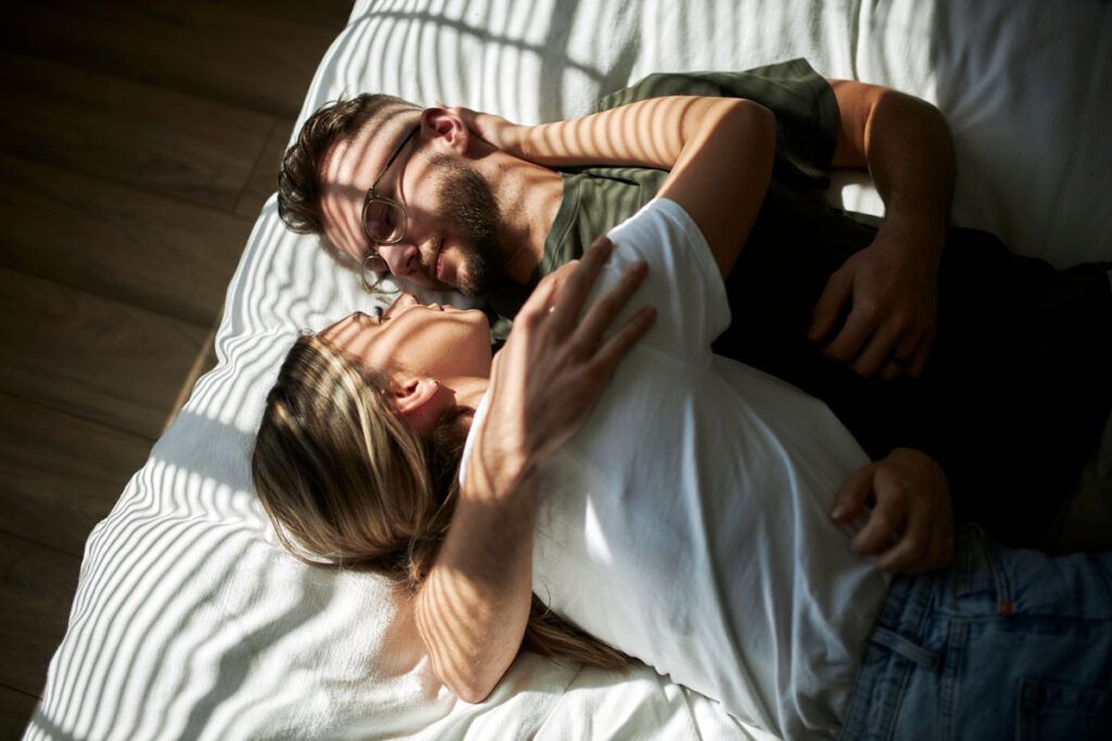A young couple lying on a mattress in each other's arms, representing HPV in males and how long it lasts.