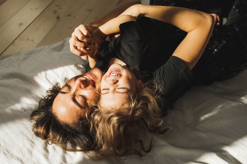 Adult female and young girl laying down and laughing in an embrace.