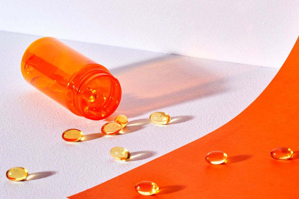 A tipped over orange pill bottle with fish oil pills scattered around it. 