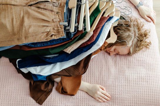A person sleeping under a pile of clothes to represent the tiredness that shingles can cause.