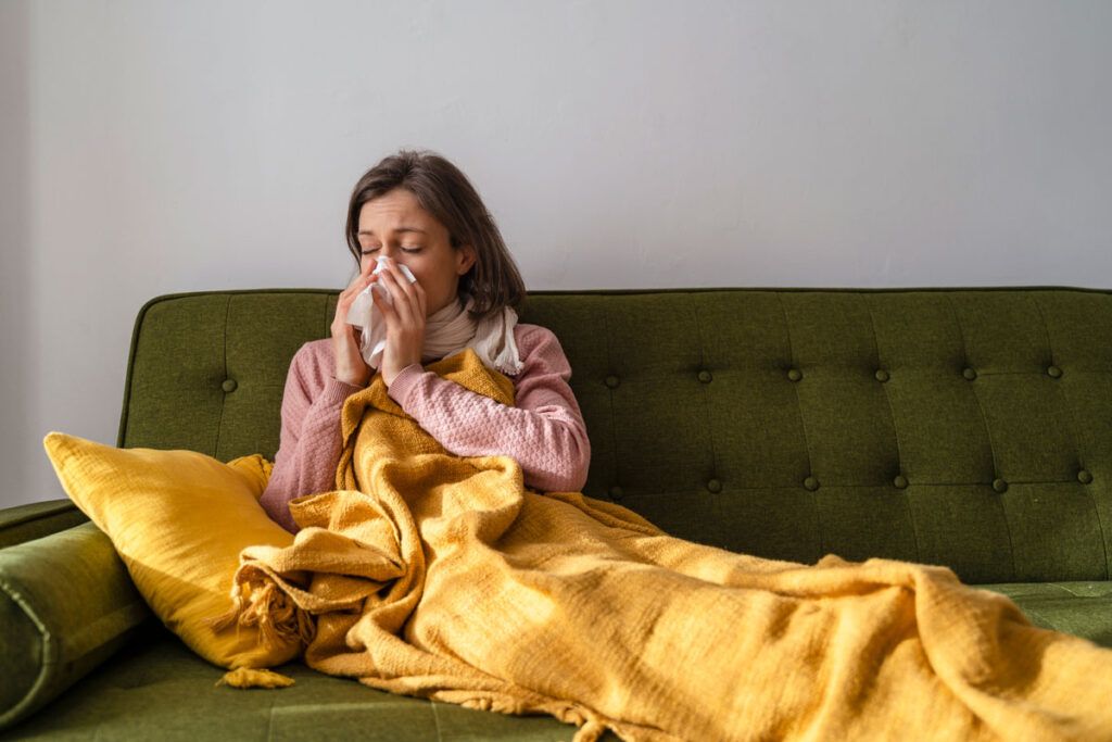 Woman in a couch taking medications for a runny nose and blowing her nose